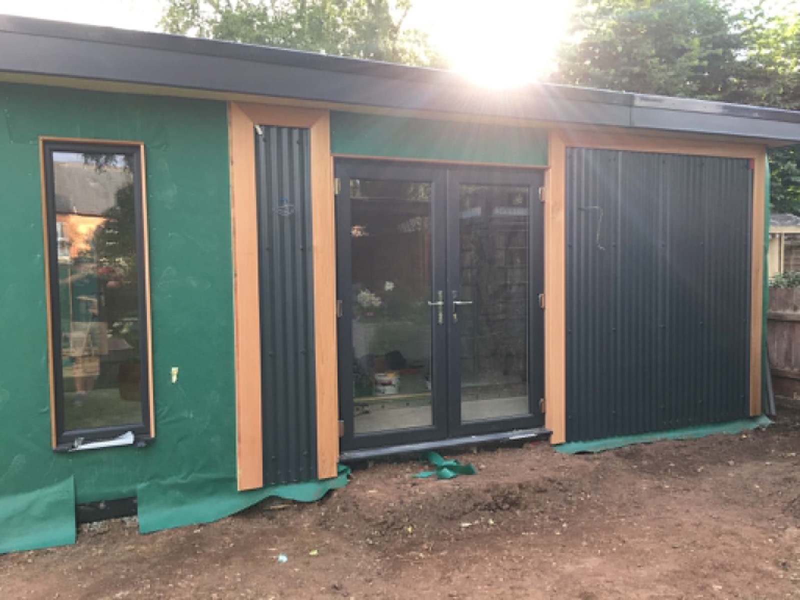 Garden room built by DJH Joinery — dark cladding, cedar trim and full-height glazing, at sunset